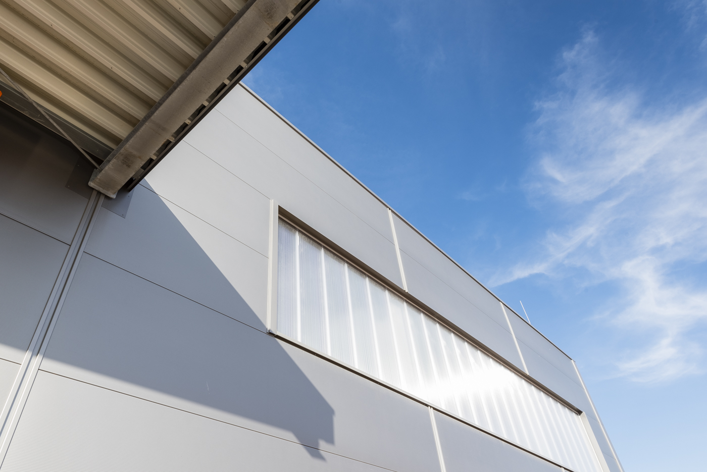 Horizontale Hoesch Sandwichfassade in RAL 9006 mit vertikalen Lisen und Polycarbonatverglasung